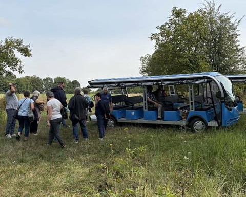 Grupa osób stoi przy niebieskim autobusie terenowym, obserwując wnętrze i przygotowania do wyjazdu.
